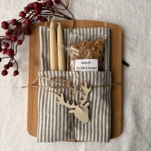 striped kitchen towel, toffee in package, 2 beeswax candles on a wood cutting board